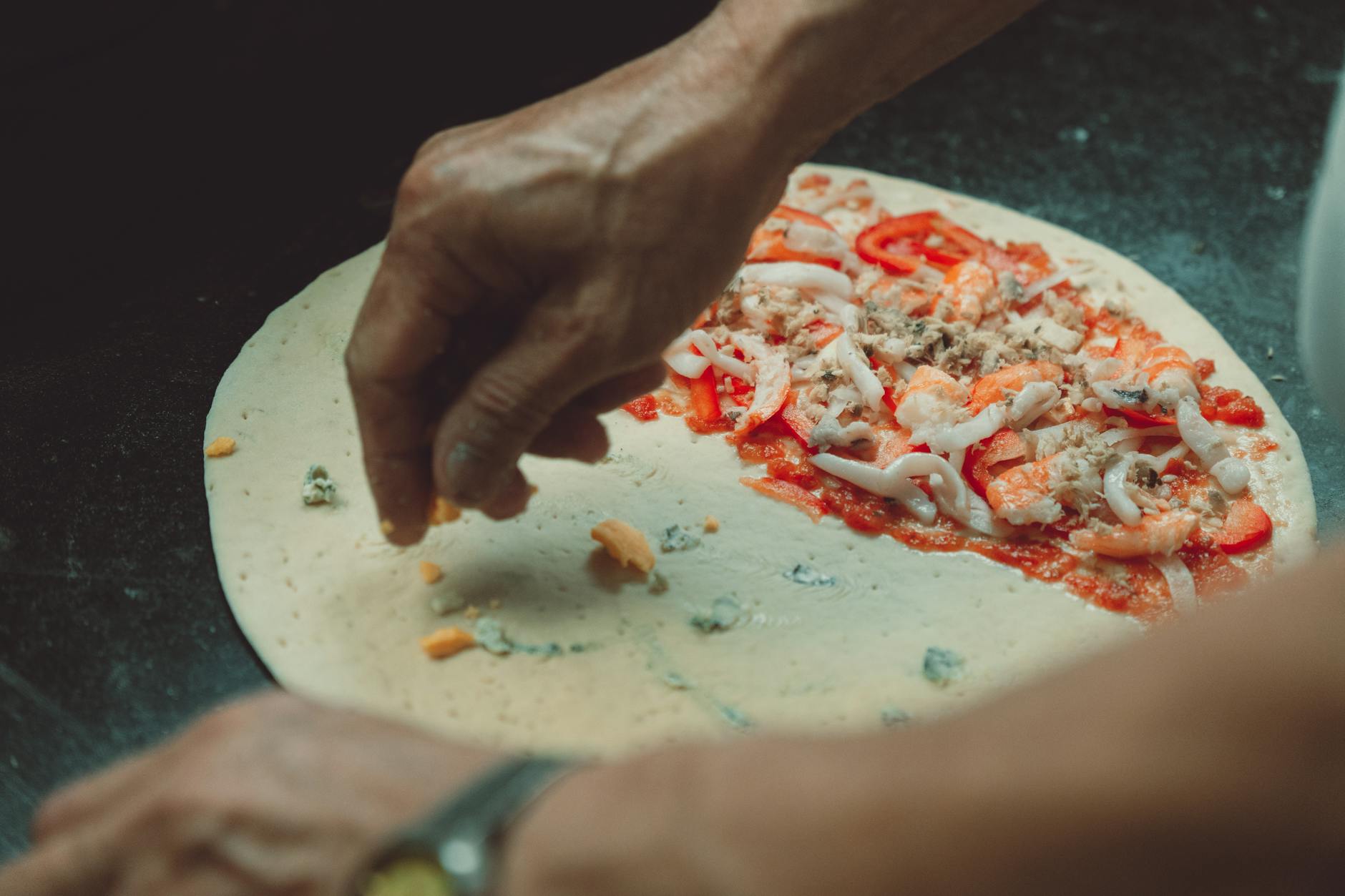 Dłonie układające świeże owoce morza na pizzy w kuchni