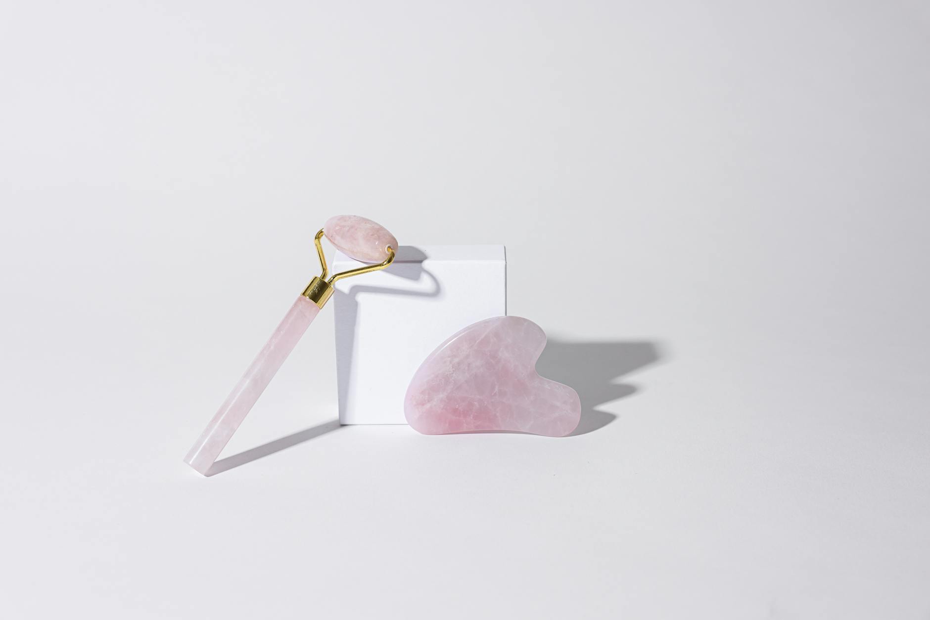 Różowy kwarcowy roller i płytka gua sha na białym tle