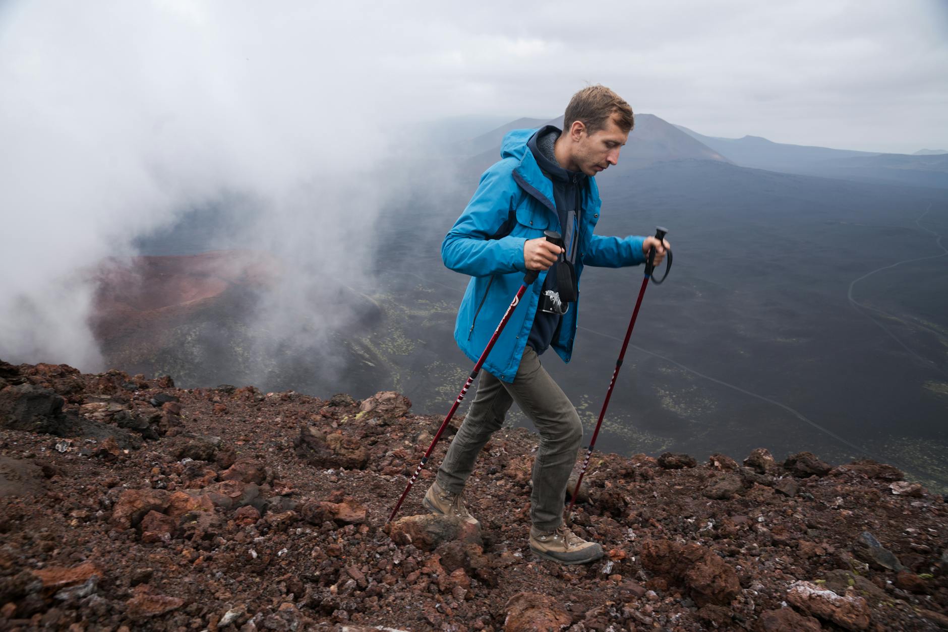 Turysta z kijkami wędruje po mglistym, skalistym zboczu wulkanu