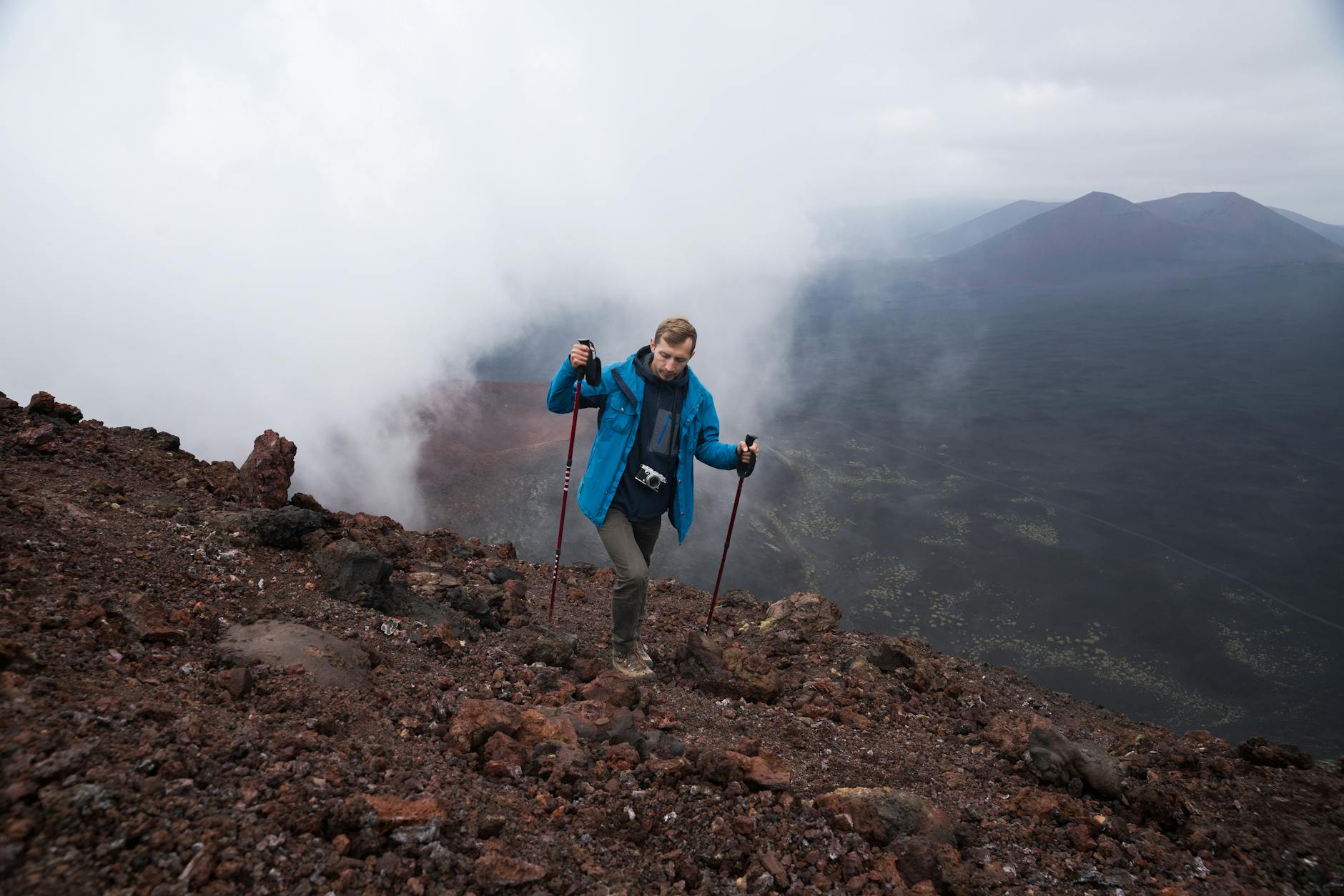 Turysta z kijkami wspina się po mglistej, skalistej zboczu wulkanu