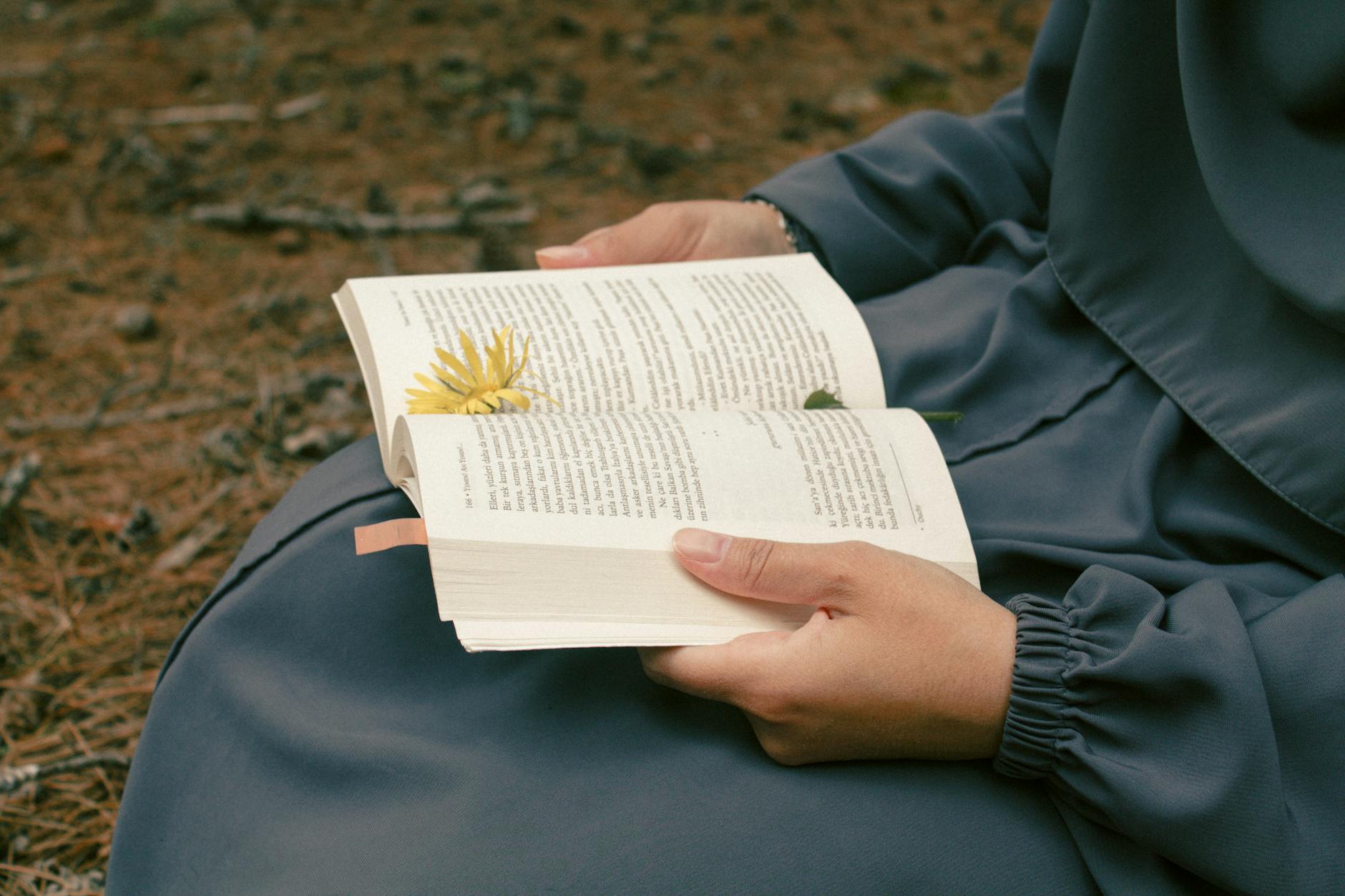 Osoba czyta książkę na świeżym powietrzu z żółtym kwiatem obok
