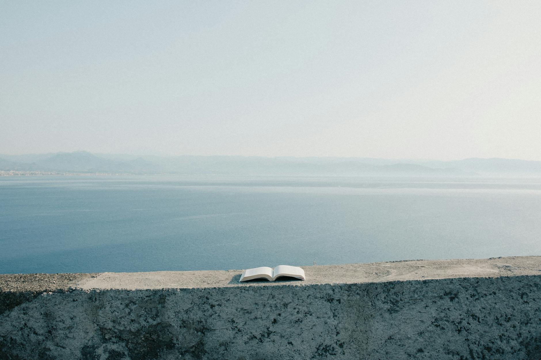 Otwarta księga na murku z widokiem na spokojne morze i niebo