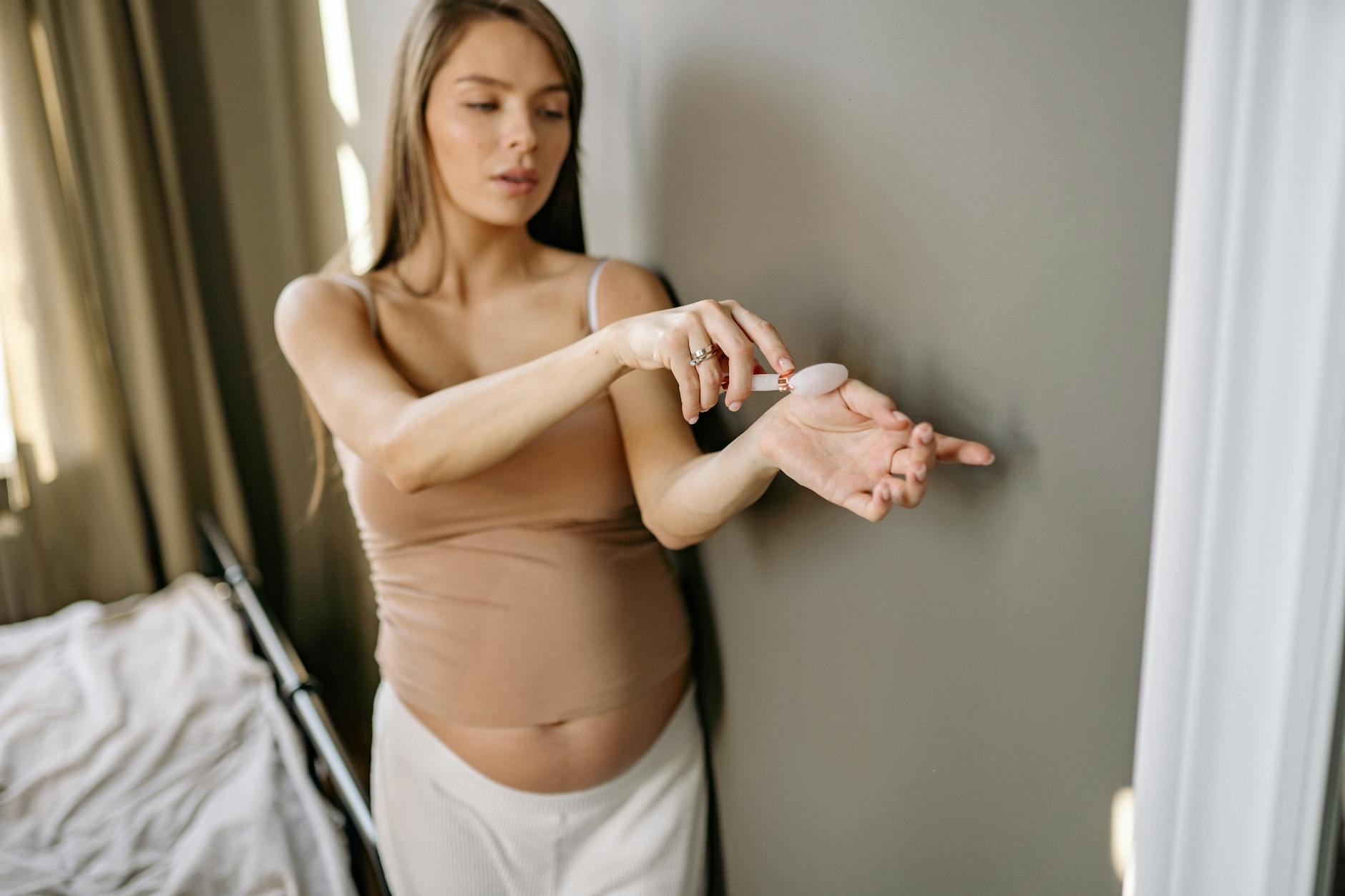 Ciężarna kobieta w sypialni masuje twarz jadeitowym rollerem dla relaksu