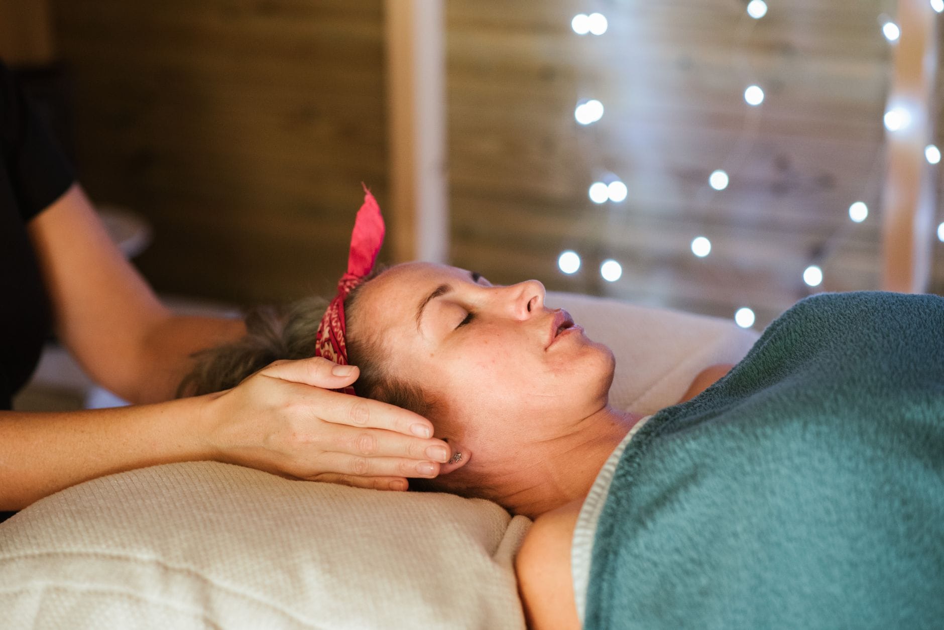 Kobieta z migreną leży pod kocem, terapeuta wykonuje masaż klasyczny