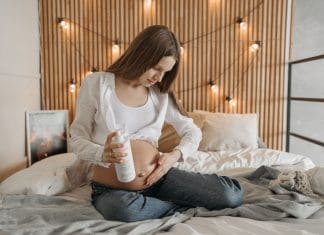 Kobieta w ciąży nakłada balsam na brzuch w sypialni